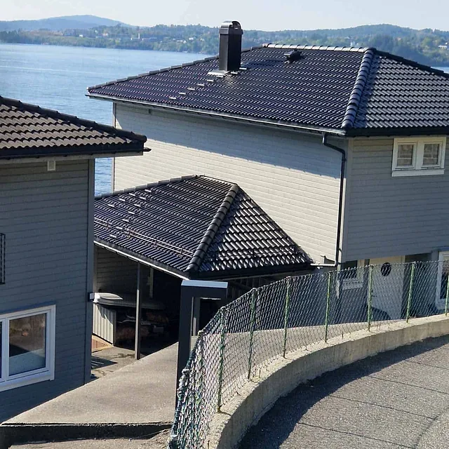 Nytt mørkt tak ferdig montert på hus med grå fasade, sett fra veien utenfor.