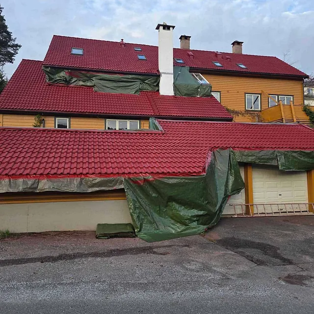 Hus med nytt rødt tak, deler dekket med grønn presenning under pågående renovering.