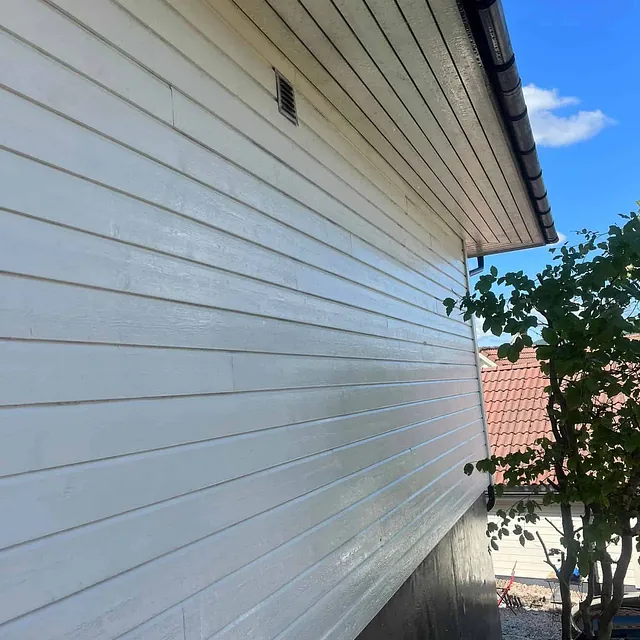 Nymalt hvit husvegg med blank overflate og mørk grunnmur, etter oppussing.